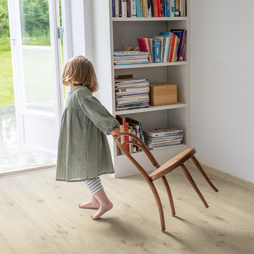 kind sleept een stoel over een grijze laminaatvloer